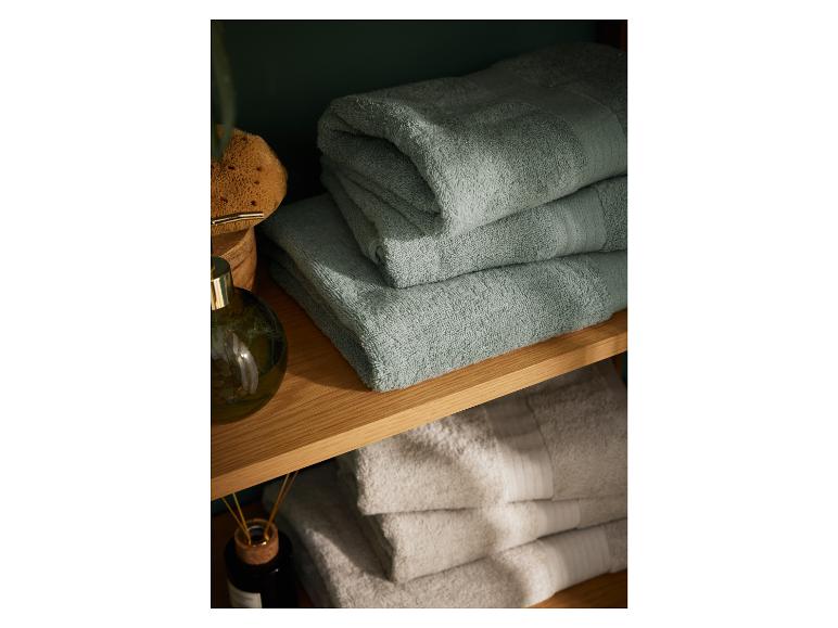 Stapel graugrüne Badetücher auf einem Holzregal.