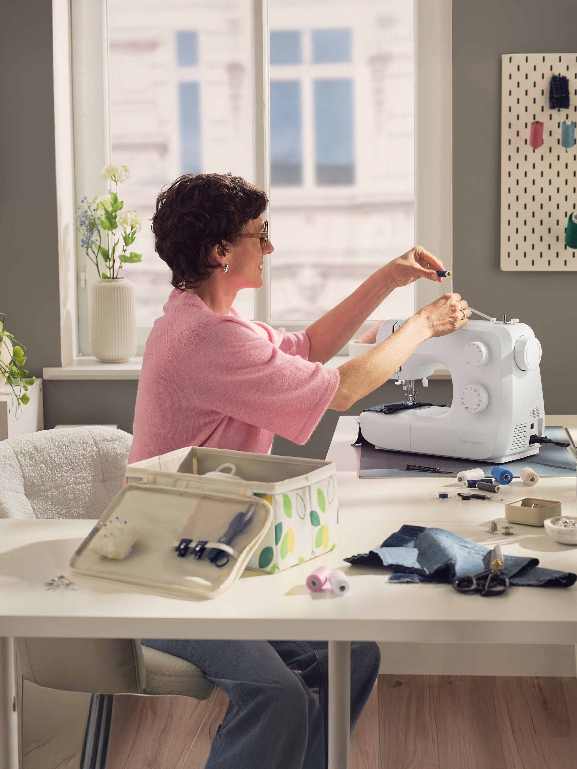 Frau näht an Nähmaschine, mit Nähzubehör auf dem Tisch.