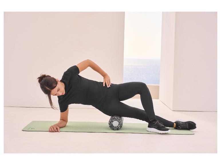 Frau in schwarzer Sportkleidung benutzt eine Faszienrolle auf einer Yogamatte.