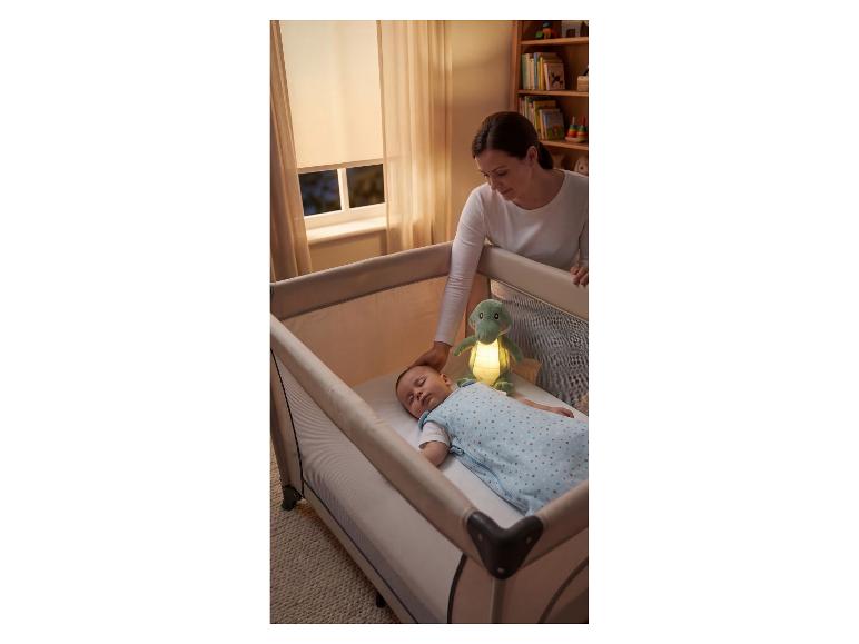 Mutter legt Baby in Reisebett mit leuchtendem Kuscheltier.