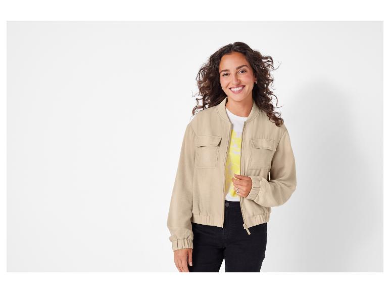 Eine Frau trägt eine beige Bomberjacke mit einem weißen T-Shirt darunter.