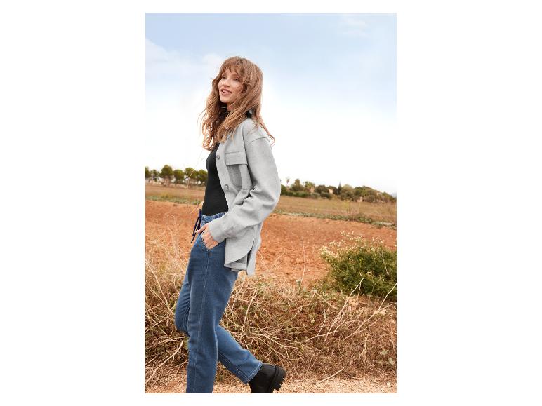 Eine Frau trägt eine graue Hemdjacke, blaue Jeans und schwarze Stiefel.