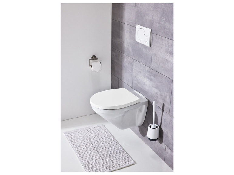 Eine weiße Toilette mit integriertem Toilettensitz, einer Toilettenbürste und einer Badematte.