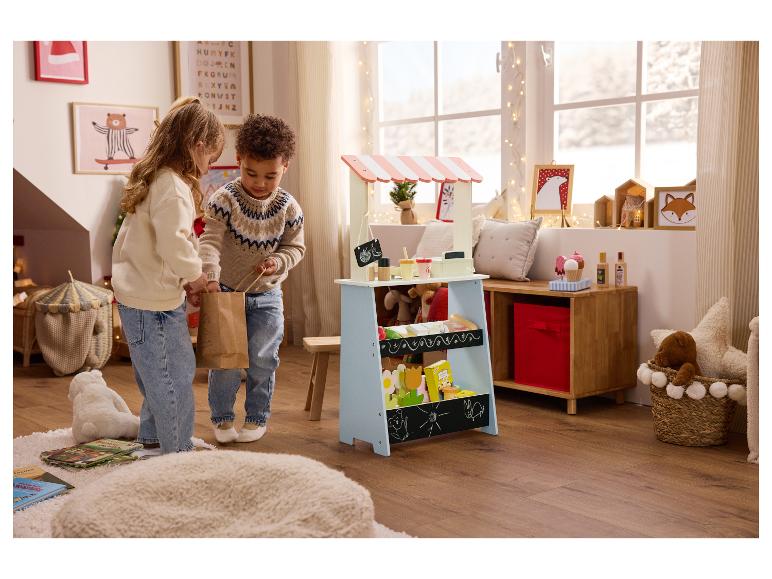 Zwei Kinder spielen mit einem Holzmarktstand und Spielzeug in einem festlich dekorierten Raum.