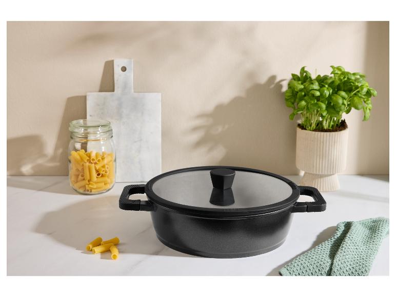 Schwarzer Topf mit Deckel, Nudeln im Glas und Basilikum auf einer Küchenarbeitsplatte.