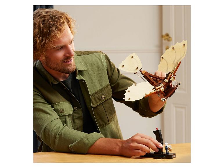 Ein Mann lächelt, während er ein Flugmaschinenmodell aus Bausteinen hält.