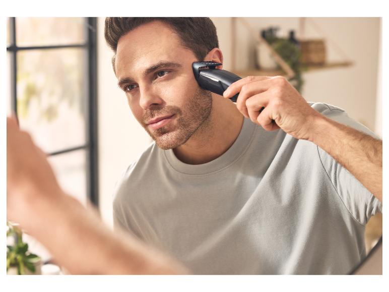 Mann rasiert sich mit einem elektrischen Trimmer und schaut in den Spiegel.