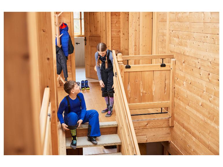 Zwei Kinder in Skikleidung, ein Junge sitzt auf der Treppe und ein Mädchen steht, bereit zum Skifahren.
