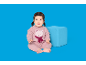 Baby in rosa Schlafanzug mit Teddybär und Schal, sitzt neben einem blauen Würfel.