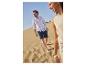Mann in weißem Hemd und dunkelblauen Shorts geht auf einer Sanddüne.