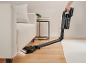 Kabelloser Staubsauger saugt Staub unter dem Sofa im Wohnzimmer.