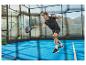 Padelspieler auf dem Platz, in schwarzer Sportkleidung, schlägt den Ball mit dem Schläger.