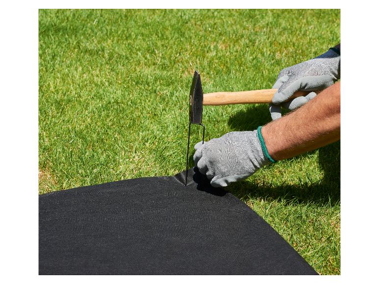 Behandschuhte Hände schlagen einen Hering mit einem Hammer in schwarzes Unkrautvlies.