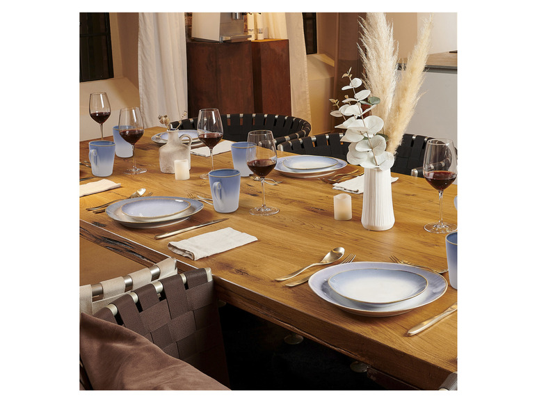 Ein Tisch gedeckt mit blauem Geschirr, Weingläsern und Keramikbechern.