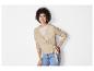 Eine Frau trägt einen beigefarbenen Pullover mit Knöpfen und blaue Jeans.