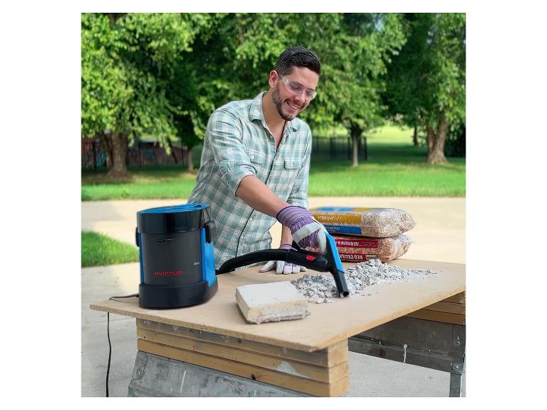 Mann benutzt einen Invictus Staubsauger, um Schutt auf einer Werkbank im Freien zu beseitigen.