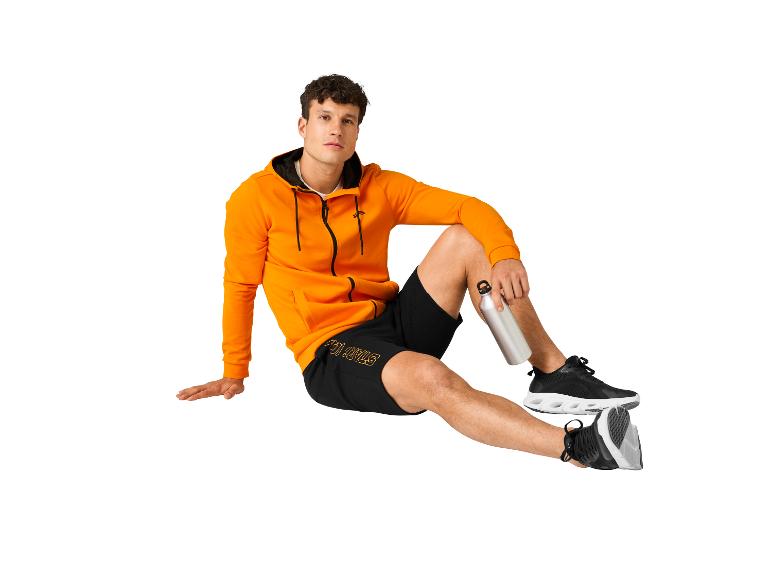 Orangene Kapuzenjacke, schwarze Stay Strong Shorts und Sportschuhe.