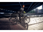 Mann in Sportkleidung mit Fahrrad unter einer Brücke, städtische Umgebung.