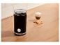 Schwarze Kaffeemühle mit Bohnen, Kaffee und Keksen auf einer Holztheke.