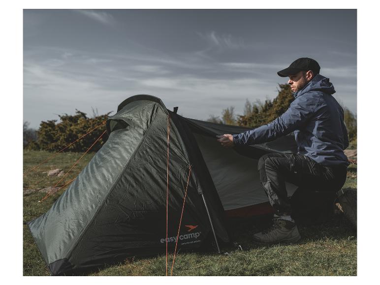 Ein Mann baut ein grünes Easy Camp-Zelt auf einer Wiese auf.