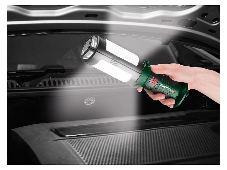 Eine Hand hält eine grüne und schwarze Arbeitsleuchte, die den Motorraum eines Autos beleuchtet.