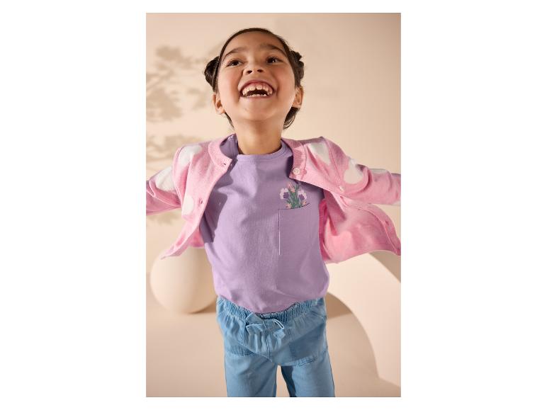 Mädchen in rosa Strickjacke und lila T-Shirt mit Blumenmuster.