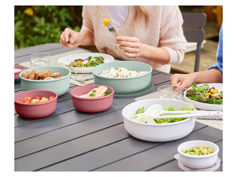 Menschen essen im Freien mit bunten Schüsseln voller Speisen auf einem grauen Tisch.