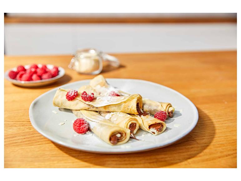 Schokoladen-Crêpes mit Himbeeren und Puderzucker auf einem Holztisch.