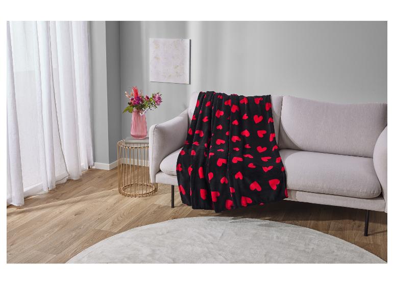 Eine schwarze Decke mit roten Herzen auf einem grauen Sofa.