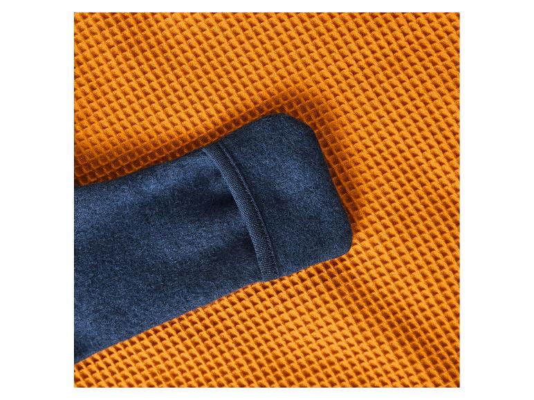 Ärmel eines blauen Wollpullovers auf einer orangefarbenen Waffeldecke.