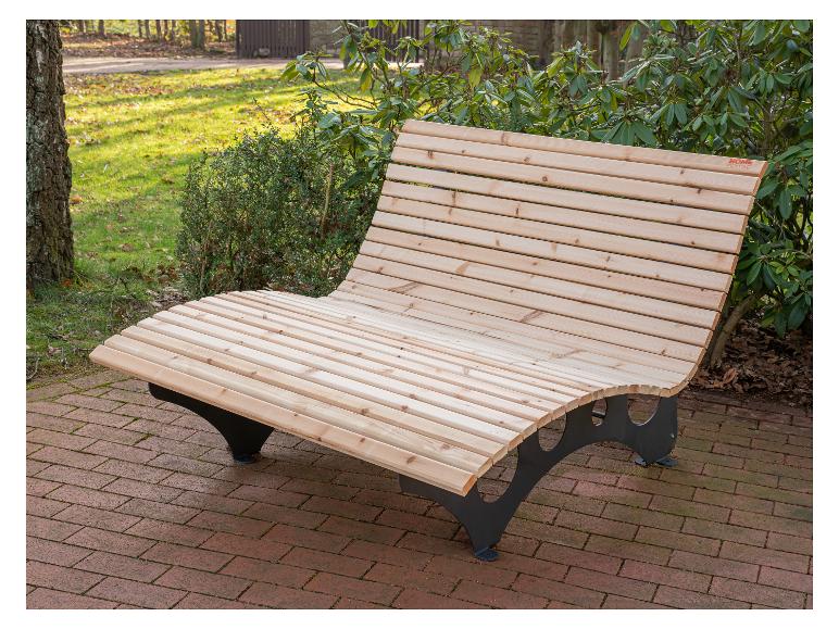 Geschwungene Holzgartenbank mit schwarzen Metallbeinen auf einem Ziegelweg.