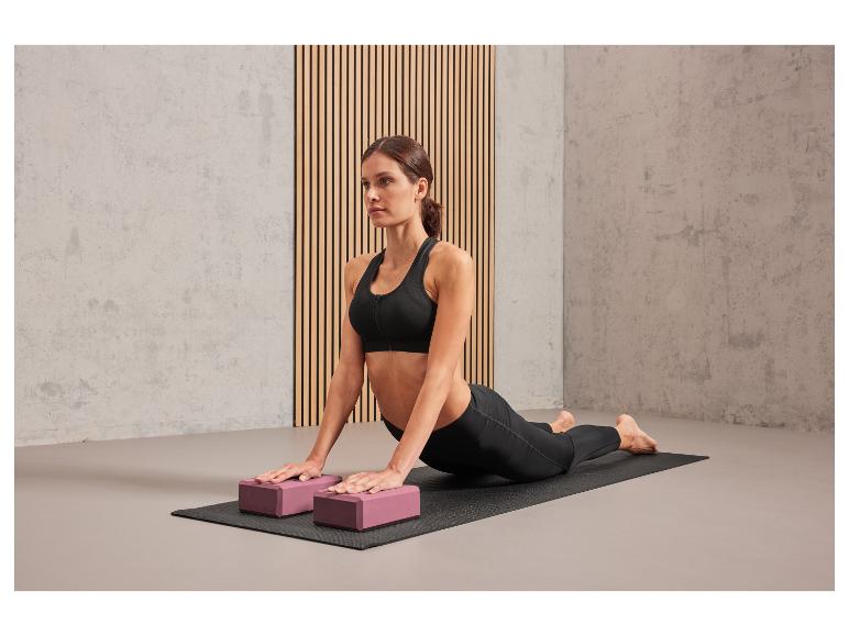Eine Frau macht Yoga auf einer Matte mit zwei rosafarbenen Blöcken.