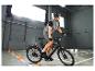 Radfahrer mit Helm und reflektierender Weste auf einem schwarzen E-Bike, der orangefarbene Hütchen umfährt.