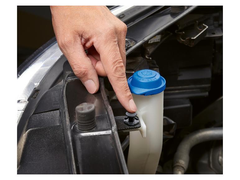 Eine Hand drückt einen schwarzen Plastikclip am Scheibenwaschbehälter eines Autos.