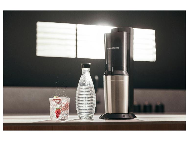 SodaStream-Gerät auf einer Arbeitsplatte, mit einer Wasserflasche und einem Glas Getränk.