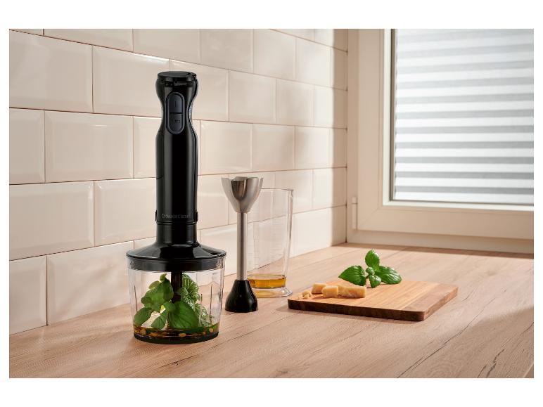 Stabmixer mit Messbecher, Basilikum, Käse und Olivenöl auf Holzarbeitsplatte.