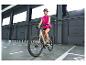 Frau in pinker Weste und Helm, fährt E-Bike in einer Halle.