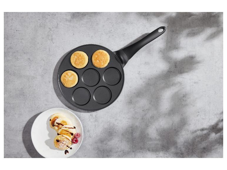 Pfanne mit Pfannkuchen und ein Teller dekorierter Pfannkuchen auf einer Betonoberfläche.