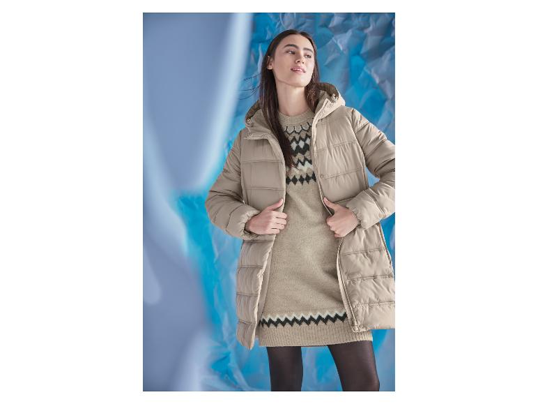 Eine Frau in einem beigen Steppmantel und einem gemusterten Strickkleid.