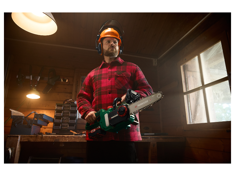 Ein Mann mit Helm und Gehörschutz hält eine Parkside Motorsäge.