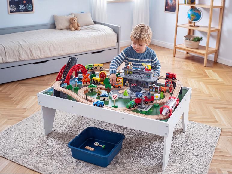 Junge spielt mit Holzeisenbahntisch mit Brücken und Gebäuden im Kinderzimmer.
