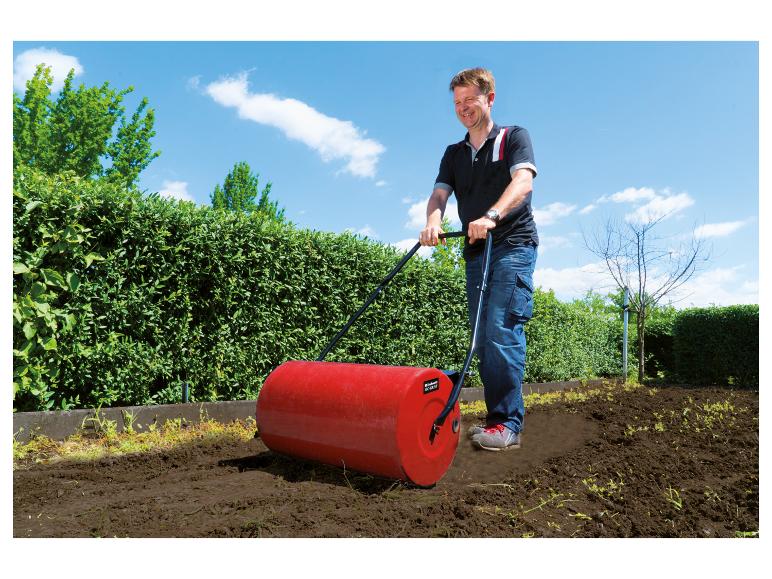 Mann walzt Erde mit einer roten Gartenwalze.