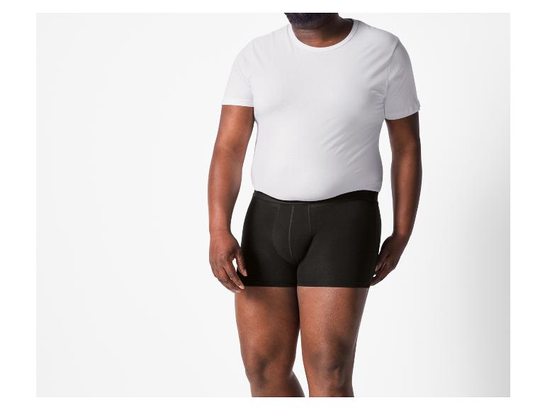 Ein Mann trägt ein weißes T-Shirt und schwarze Boxershorts.