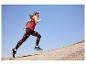 Frau läuft in rotem Tanktop und gemusterten Leggings vor blauem Himmel.
