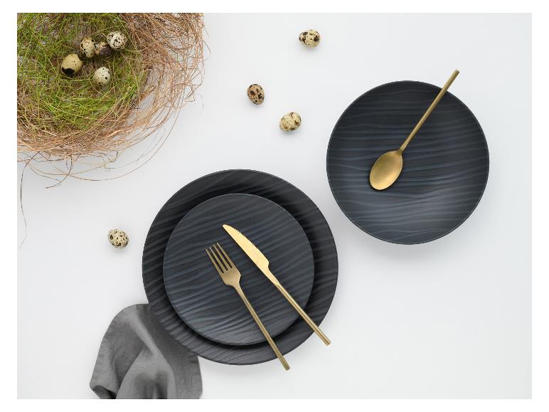 Schwarze Teller mit goldenem Besteck, Wachteleiern und einem Nest auf weißem Hintergrund.