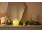 Festliche Weihnachtsdekoration mit einer leuchtenden Kugel, kleinen Bäumchen und Tannengrün auf einer Kommode.