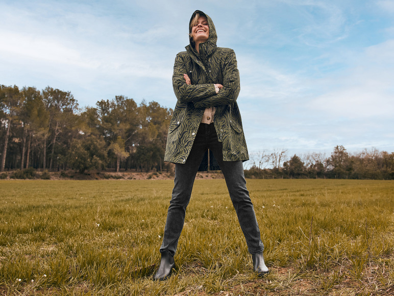 Eine Frau in einer grünen Jacke mit Leopardenmuster auf einer Wiese.