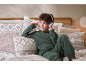 Junge im grünen Fleece-Pyjama hört mit Kopfhörern Musik im Bett.