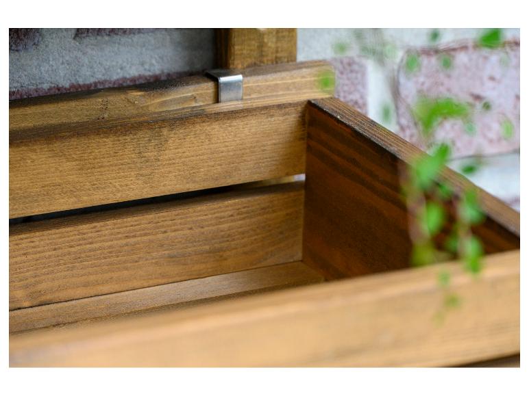 Holzaufbewahrungsbox oder Blumentopf mit Pflanzen im Hintergrund.