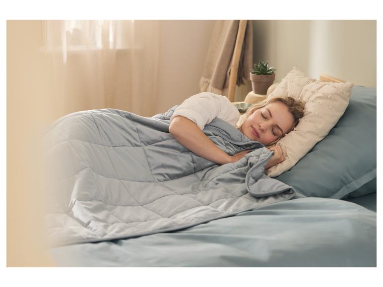Frau schläft friedlich im Bett unter einer grauen Gewichtsdecke.